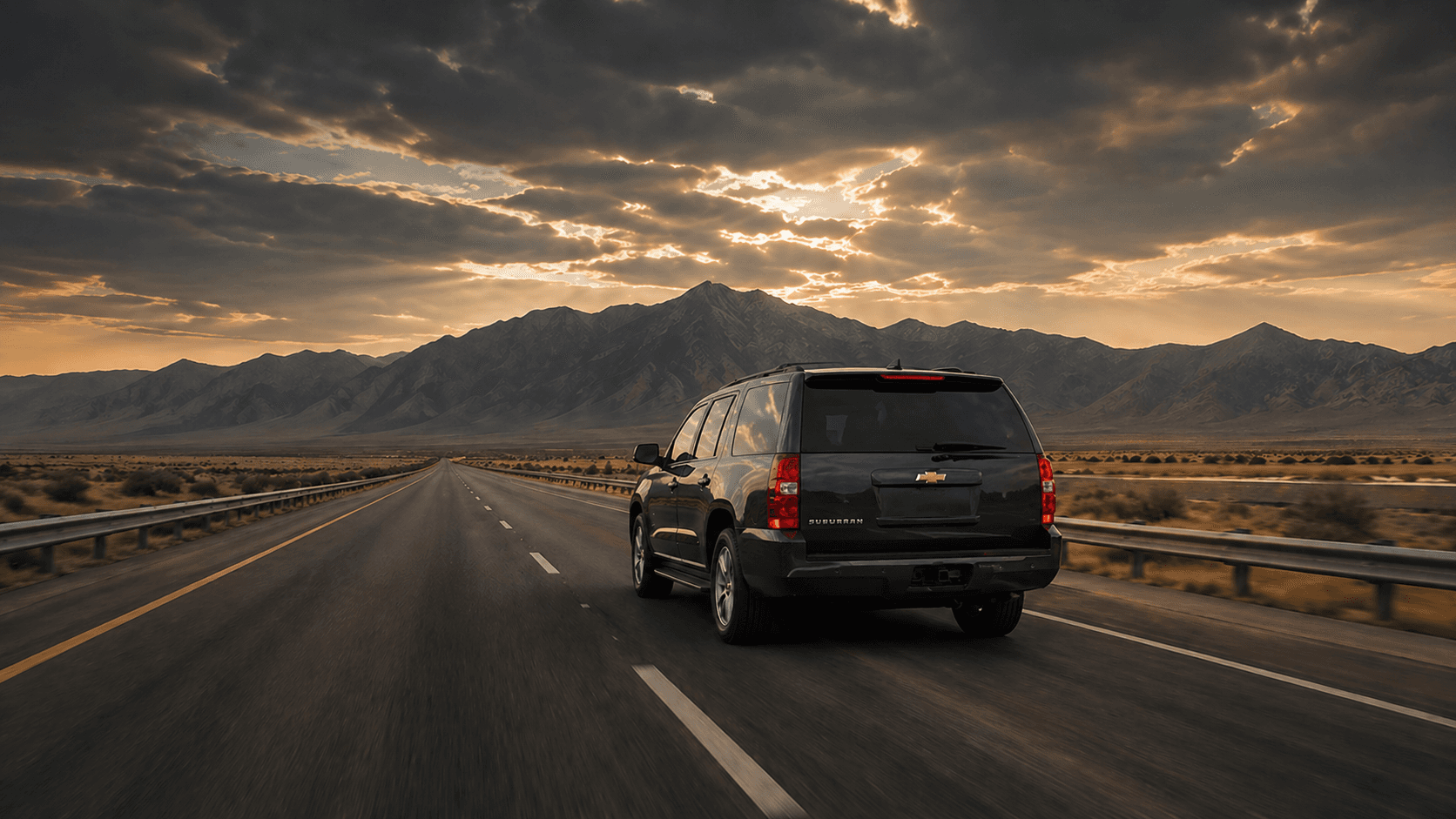 Black luxury SUV driving on an open western highway at sunset
